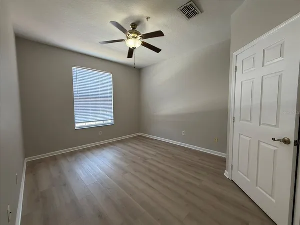 an empty room with wooden floor chandelier fan and windows