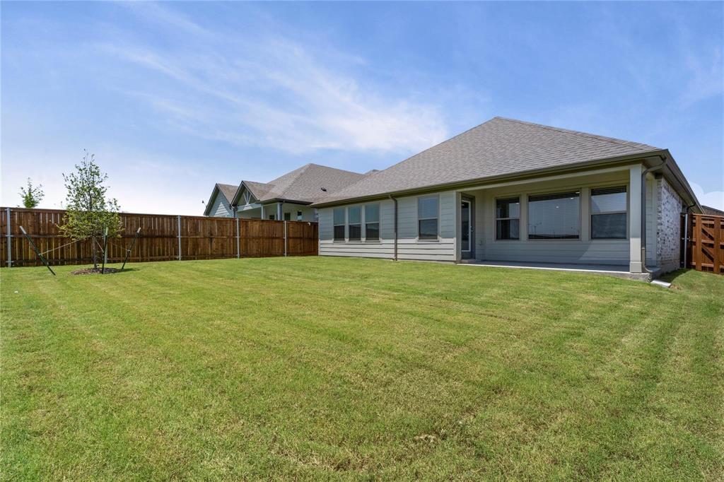 507 Avocet Road Princeton, TX 75407 - Photo 28 of 31 Expansive backyard featuring a manicured lawn, wood privacy fencing, a covered concrete patio, and a light-colored exterior with multiple windows