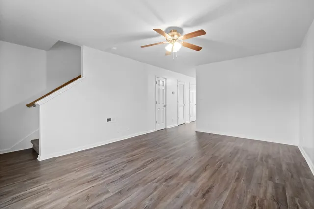 a view of an empty room with wooden floor and a chandelier fan