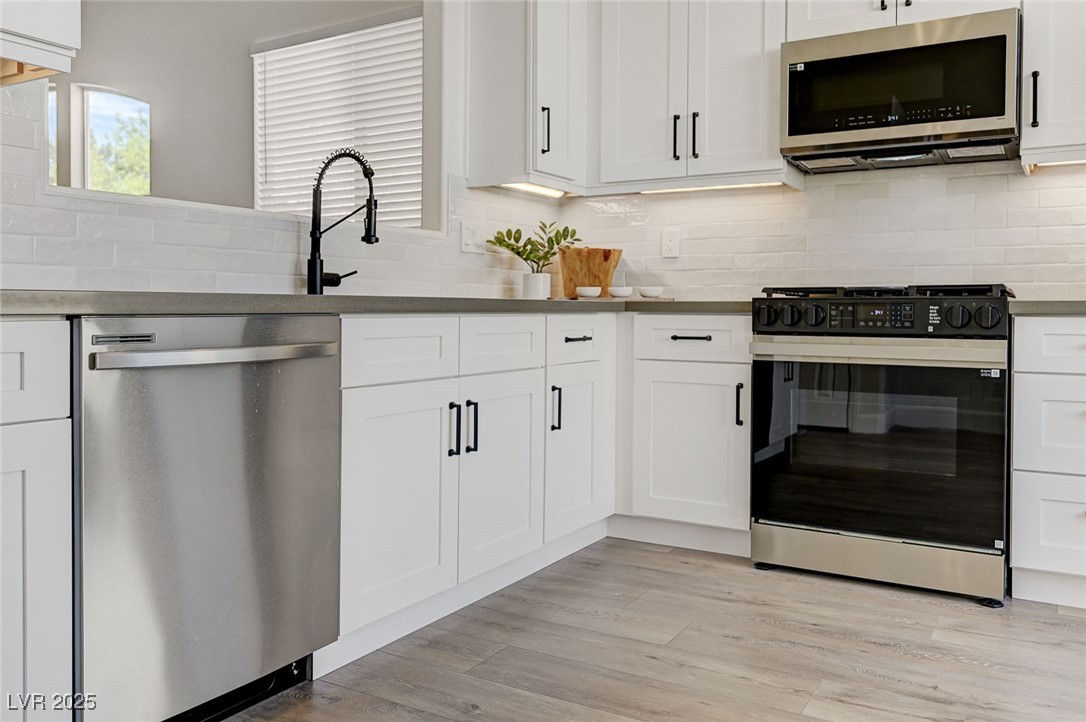 1995 Thunder Ridge Circle Henderson, NV 89012 - Photo 11 of 47 Kitchen featuring light wood finished floors, stainless steel appliances, dark countertops, white cabinets, and decorative backsplash