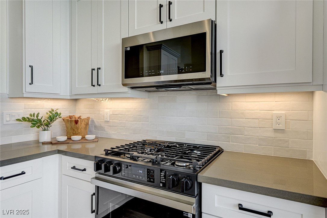 1995 Thunder Ridge Circle Henderson, NV 89012 - Photo 12 of 47 Kitchen with tasteful backsplash, gas range oven, stainless steel microwave, dark countertops, and white cabinets