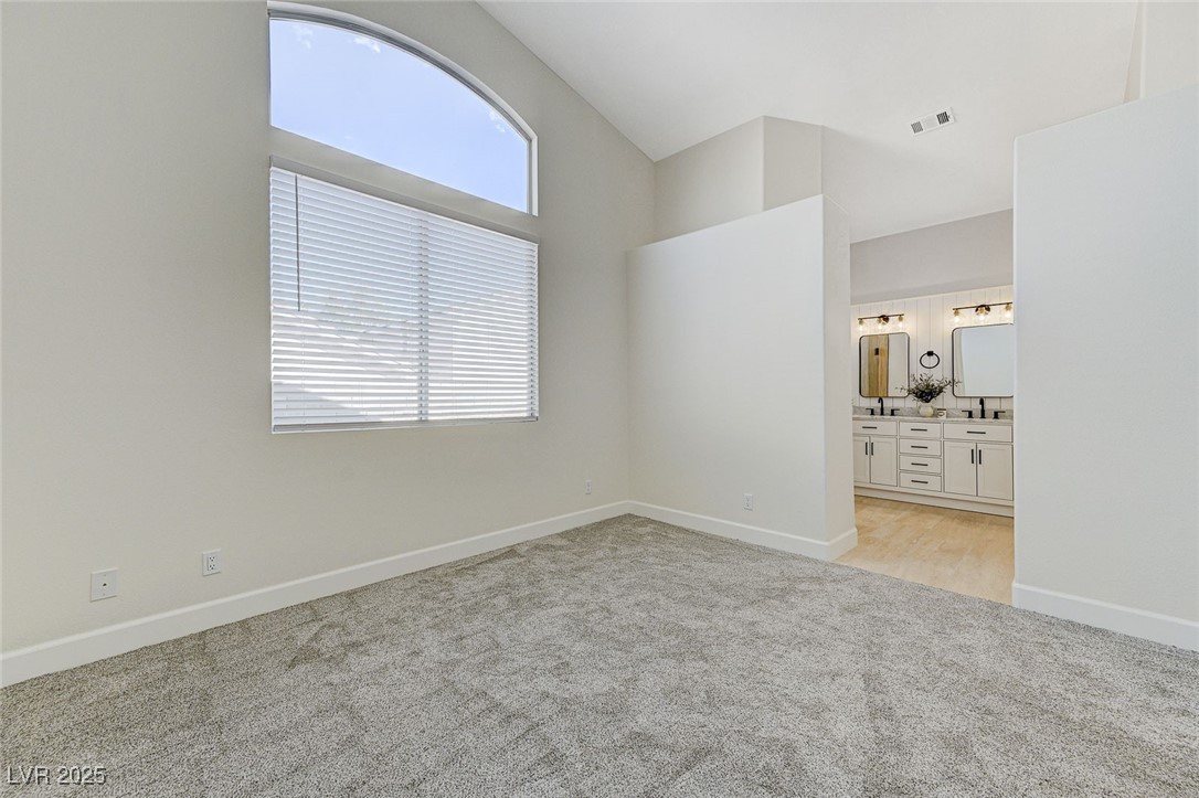 1995 Thunder Ridge Circle Henderson, NV 89012 - Photo 22 of 47 Unfurnished bedroom with high vaulted ceiling, baseboards, connected bathroom, visible vents, and light carpet