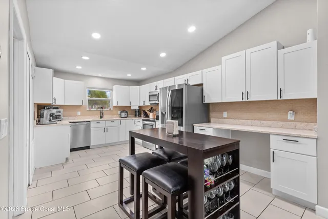 a living room with stainless steel appliances kitchen island granite countertop a table chairs and a refrigerator