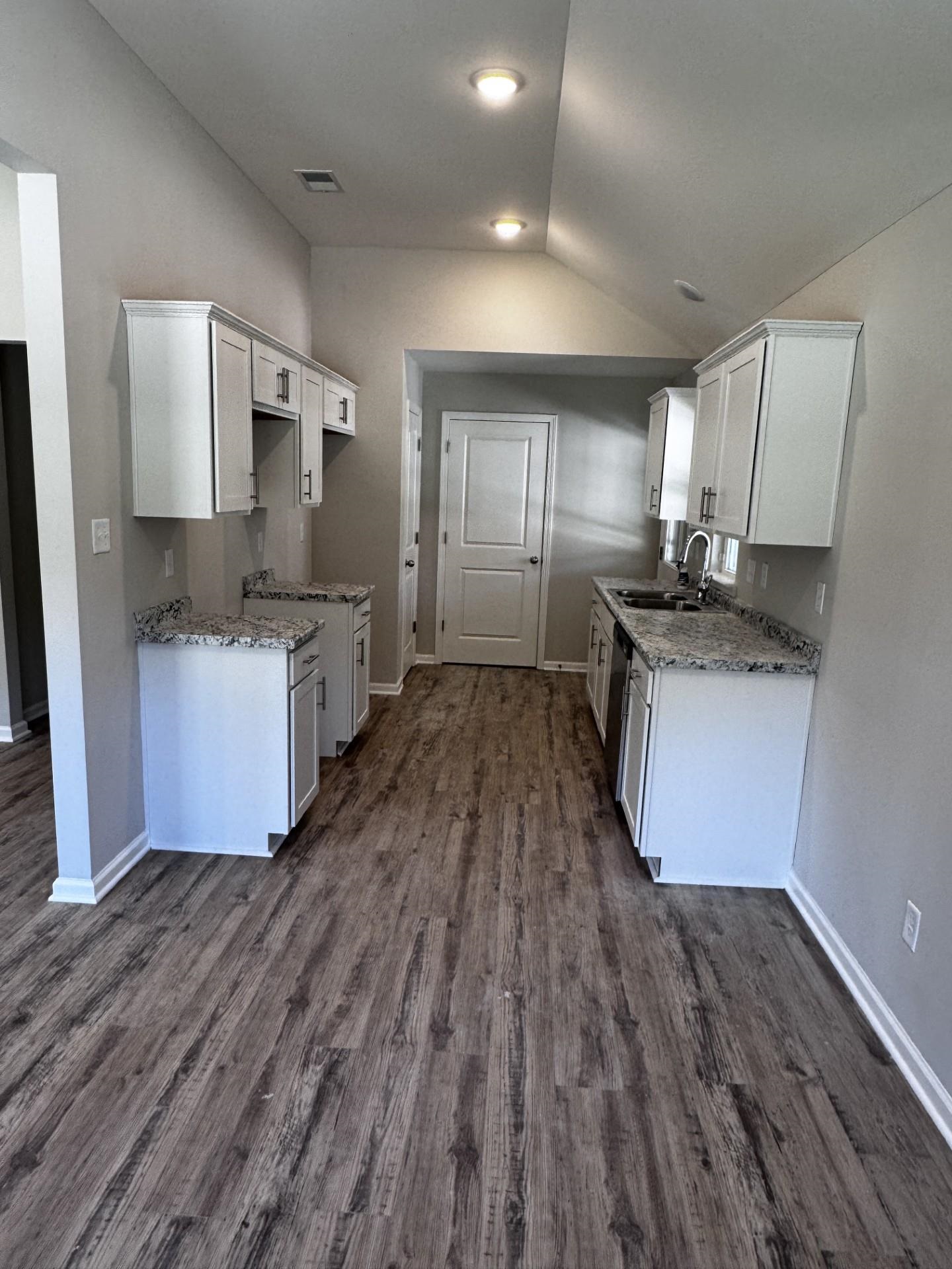 Kitchen with white cabinets, light stone countertops, vaulted ceiling, and dark wood-type flooring