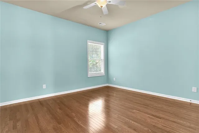 an empty room with wooden floor chandelier fan and windows
