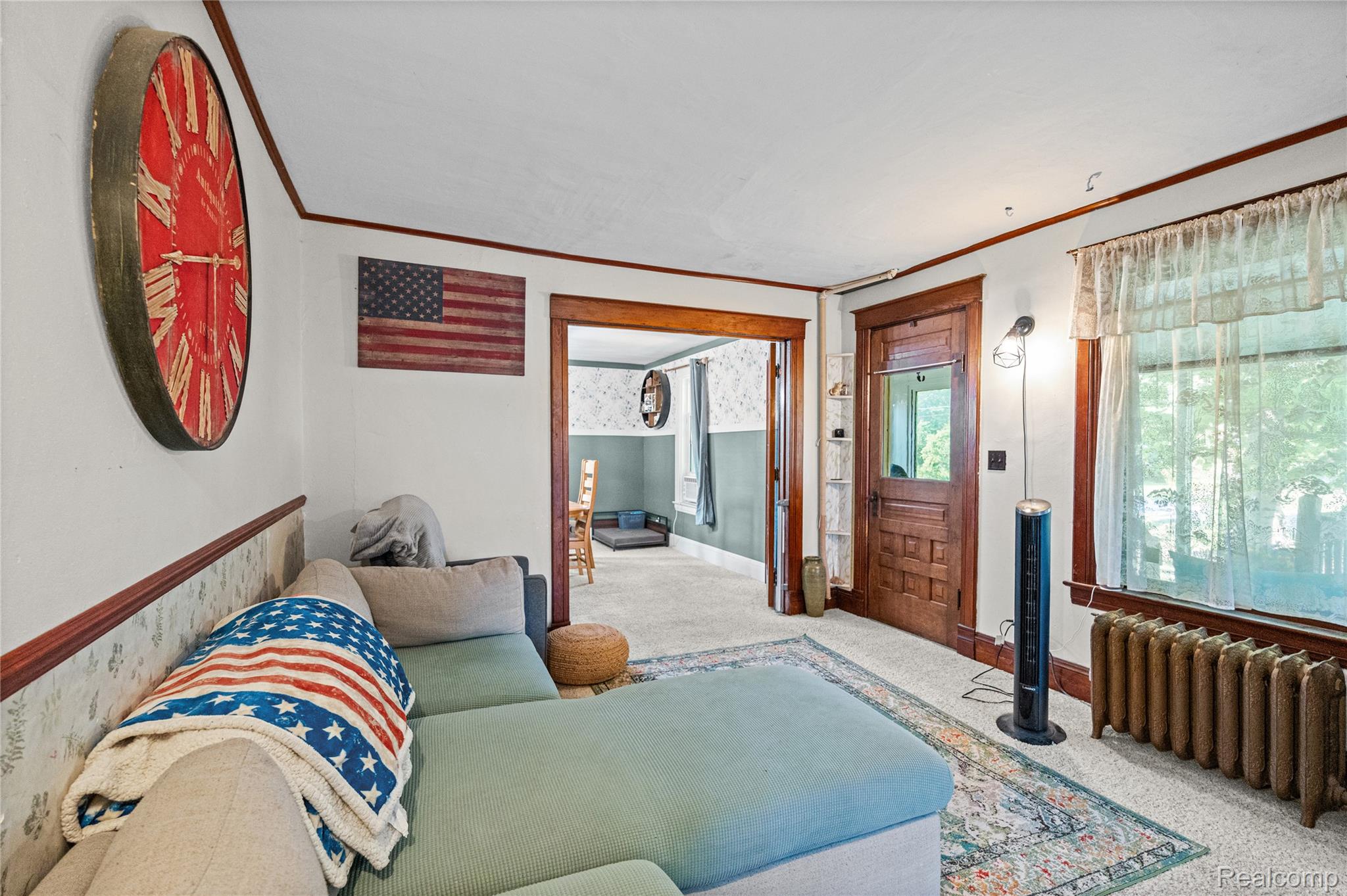 1175 South Morrish Road Flint, MI 48532 - Photo 22 of 72 Carpeted living area featuring a large window with sheer curtains, a substantial cast iron radiator, and a paneled wooden door with a glass insert