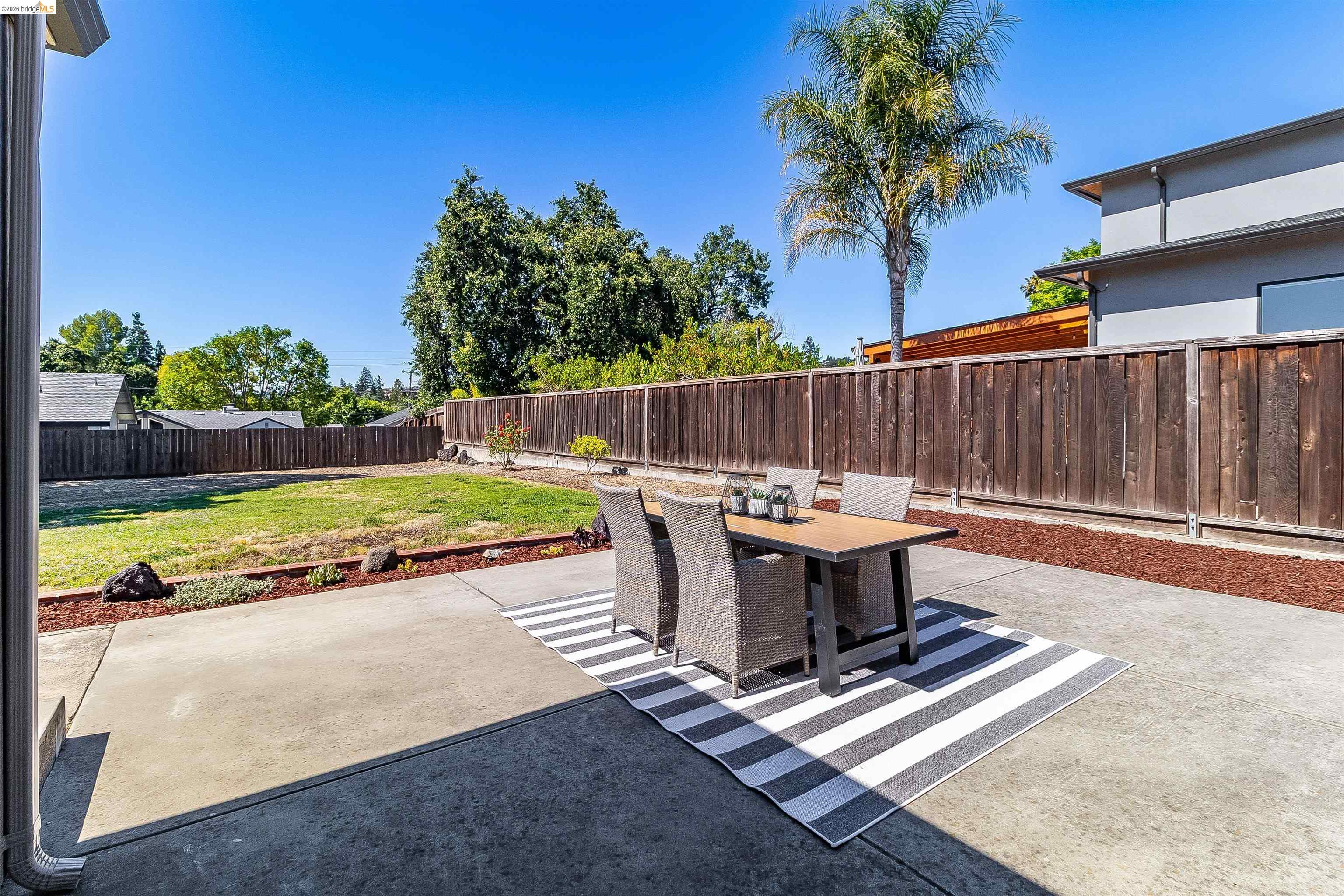 346 Valley View Road Pleasant Hill, CA 94523 - Photo 43 of 57 Spacious concrete patio featuring a wood privacy fence, expansive lawn area, mature trees, and a modern exterior building with multiple windows