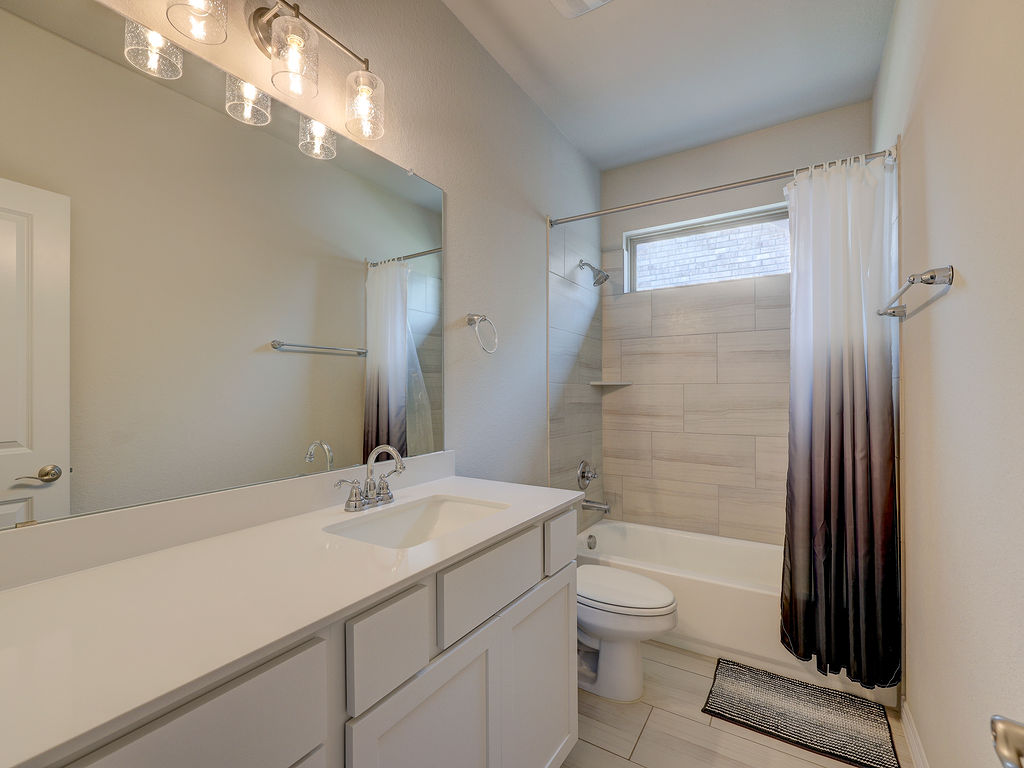 229 Heartleaf Road San Marcos, TX 78666 - Photo 33 of 40 A well-appointed bathroom features a single vanity, a spacious mirror, and a tiled shower-tub combination with a window for natural light.