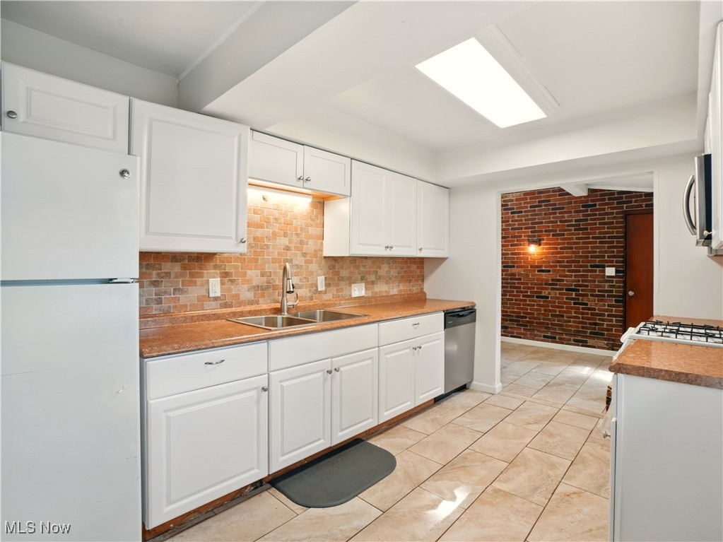 1942 Benjamin Road Madison, OH 44057 - Photo 6 of 29 Kitchen with appliances, a sink, brick wall, white cabinets, and decorative backsplash