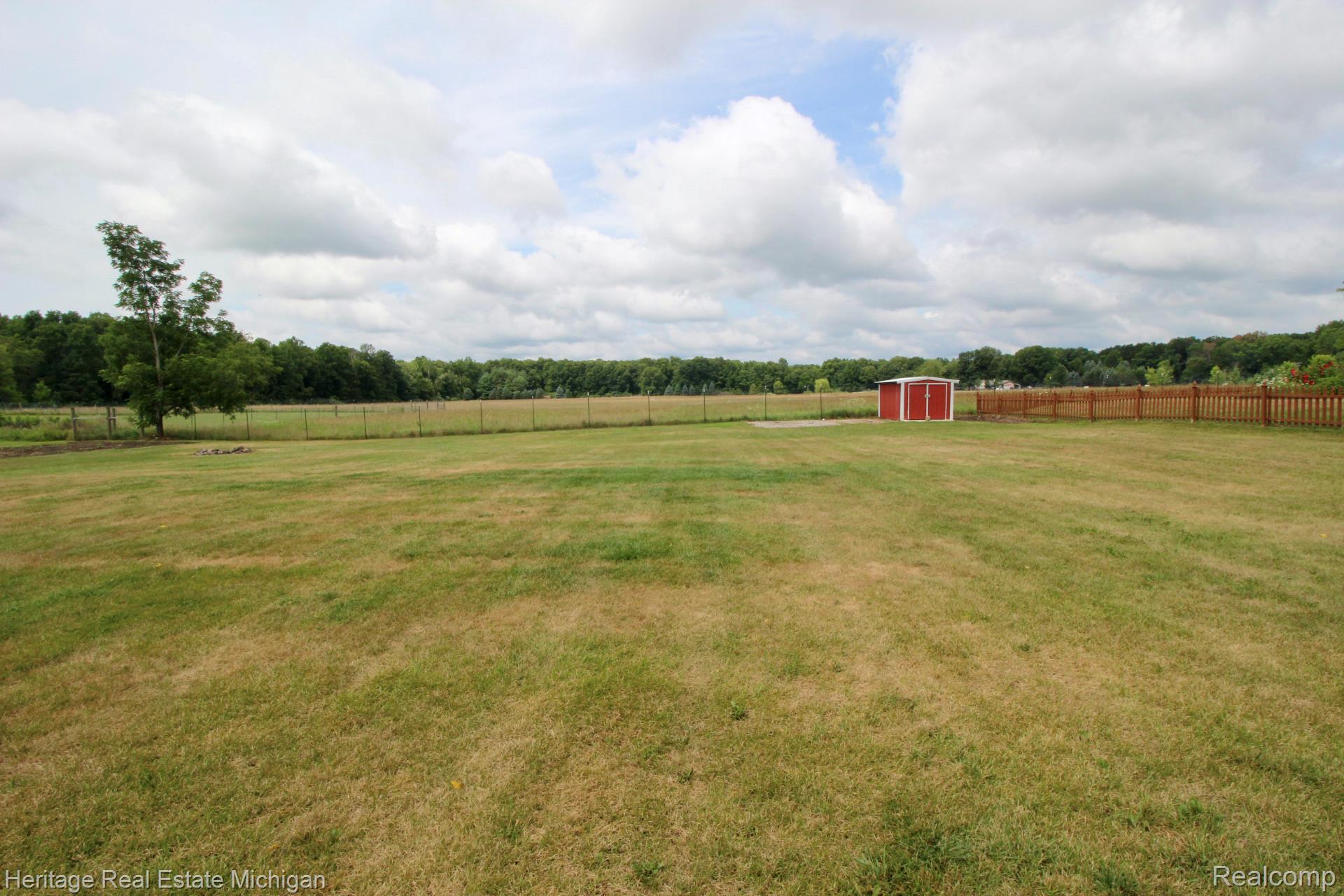 15352 South Duffield Road Byron, MI 48418 - Photo 33 of 47 Expansive grassy yard featuring a red storage shed, wood privacy fencing, and a chain-link fence bordering a treeline