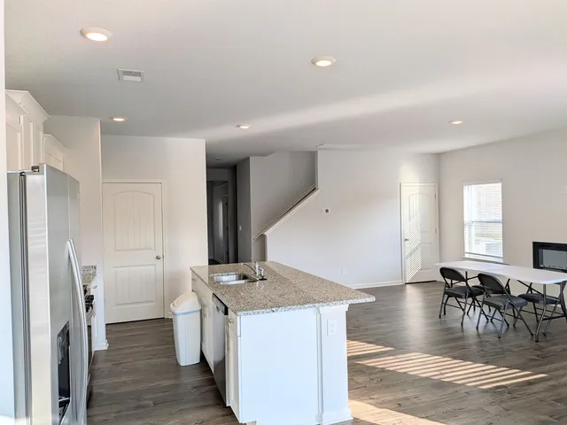 a kitchen with stainless steel appliances granite countertop a stove a sink a refrigerator and white cabinets with wooden floor