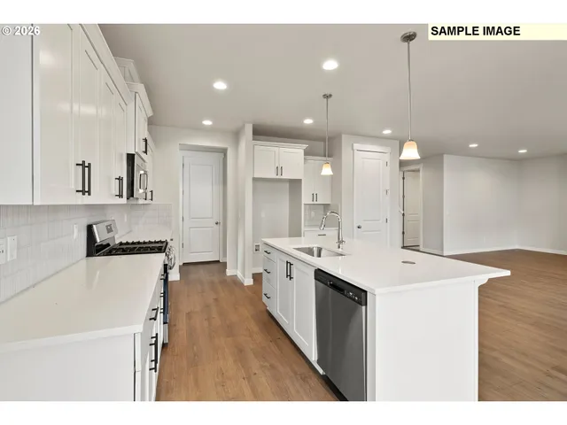 a large white kitchen with a large counter top a sink stainless steel appliances and cabinets