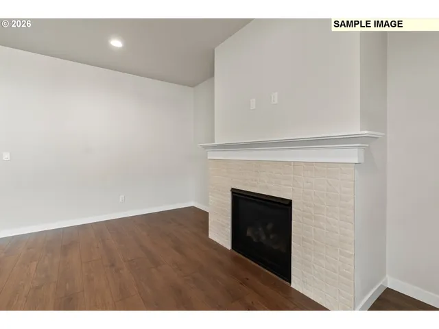 a view of an empty room with wooden floor and a fireplace