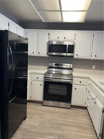 a view of a refrigerator in kitchen and an empty room with wooden floor