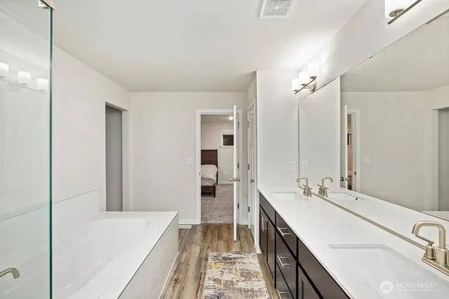 a bathroom with a double vanity sink a large mirror and a bathtub