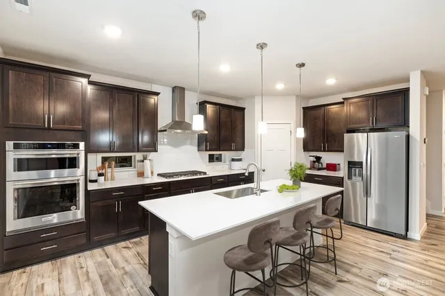 a kitchen with stainless steel appliances kitchen island granite countertop a refrigerator a stove a sink a dining table and chairs with wooden floor