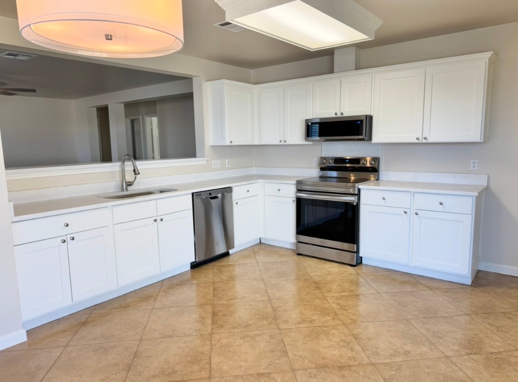 110 Comal Cove Elgin, TX 78621 - Photo 7 of 25 Kitchen featuring appliances with stainless steel finishes, light countertops, white cabinets, light tile patterned floors, and a ceiling fan