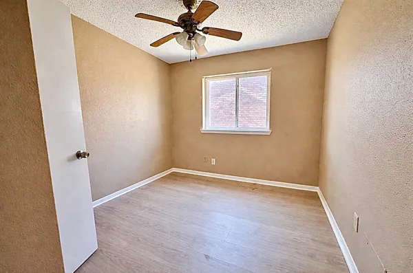 an empty room with wooden floor fan and windows
