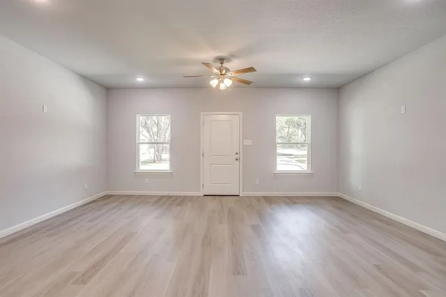 an empty room with wooden floor ceiling fan and windows