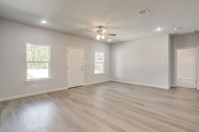 an empty room with wooden floor chandelier fan and windows