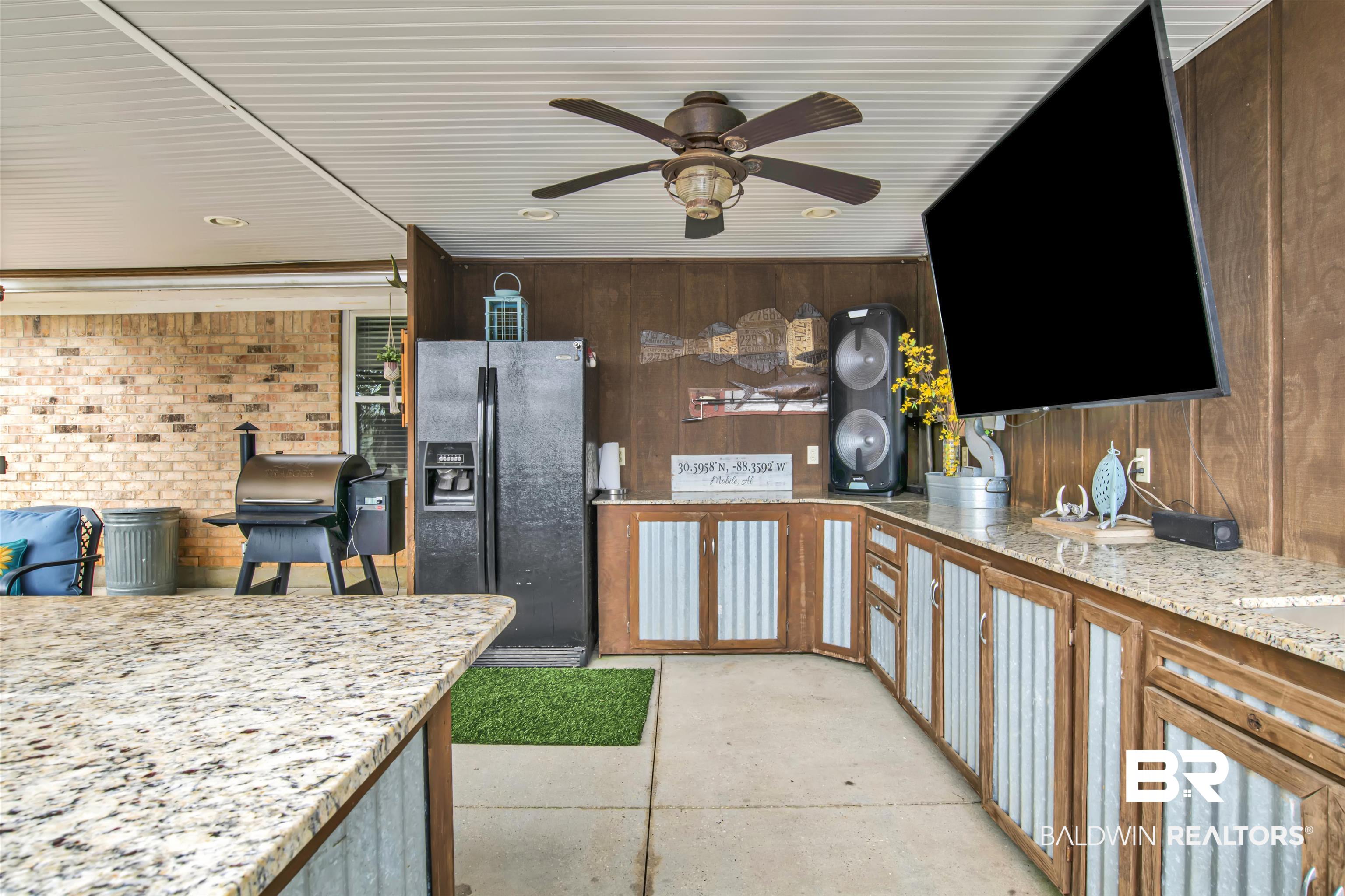 13385 Tom Gaston Road Mobile, AL 36695 - Photo 26 of 42 Kitchen with light stone countertops, wooden walls, black fridge with ice dispenser, and ceiling fan