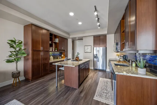 a kitchen with granite countertop a refrigerator a stove a sink dishwasher and a dining table with wooden floor