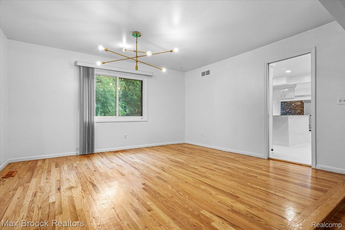 1830 Lone Pine Road Bloomfield Hills, MI 48302 - Photo 15 of 70 Hardwood flooring, contemporary brass chandelier, white walls, large window, and a clear doorway leading to a modern kitchen
