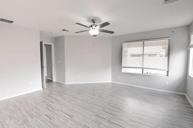 an empty room with wooden floor ceiling fan and windows