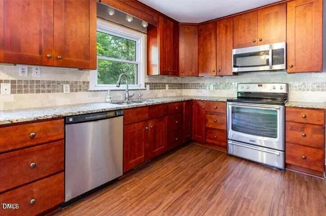 a kitchen with granite countertop wooden floors wooden cabinets stainless steel appliances a window and a sink