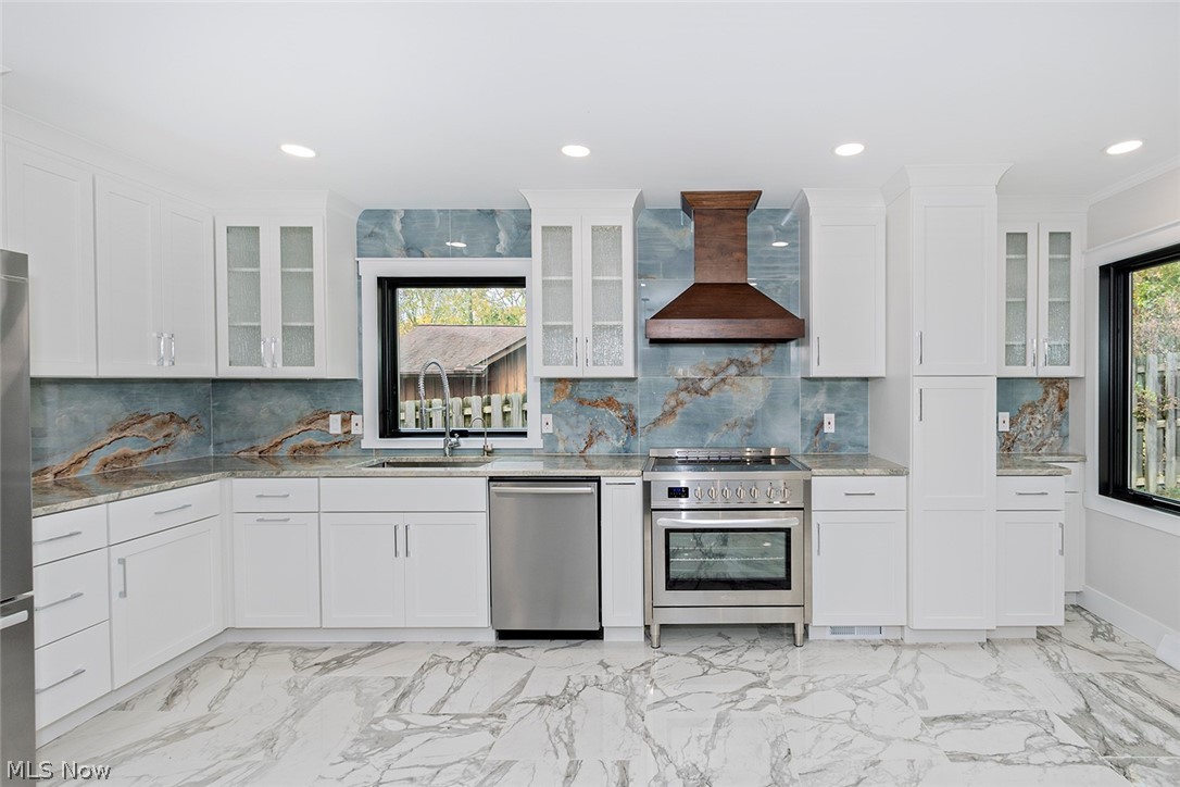20601 Shelburne Road Shaker Heights, OH 44122 - Photo 7 of 29 Kitchen with glass insert cabinets, light marble finish floors, appliances with stainless steel finishes, wall chimney exhaust hood, and recessed lighting
