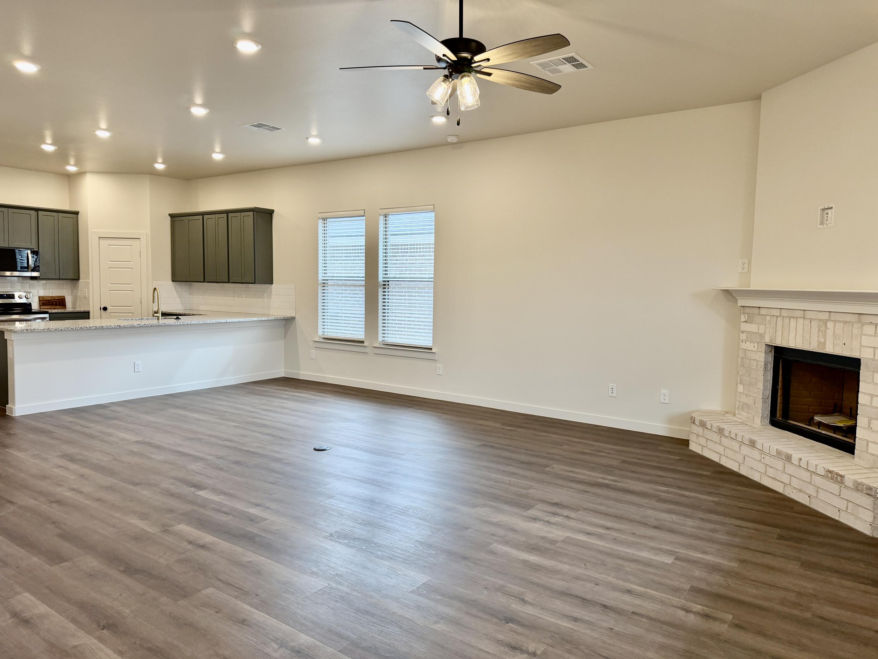 7007 16th Street Lubbock, TX 79416 - Photo 11 of 32 an empty room with wooden floor a ceiling fan a fireplace and windows