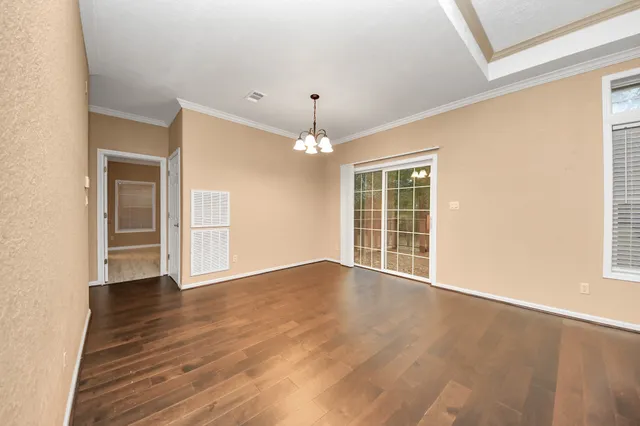 an empty room with wooden floor chandelier and windows