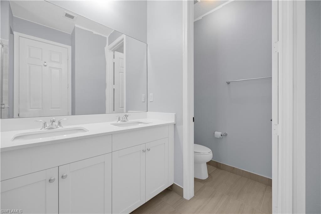 9045 Madrid Circle Naples, FL 34104 - Photo 31 of 46 a bathroom with a double vanity sink toilet and a mirror