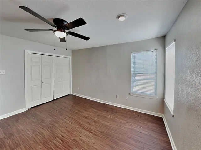 an empty room with wooden floor ceiling fan and windows