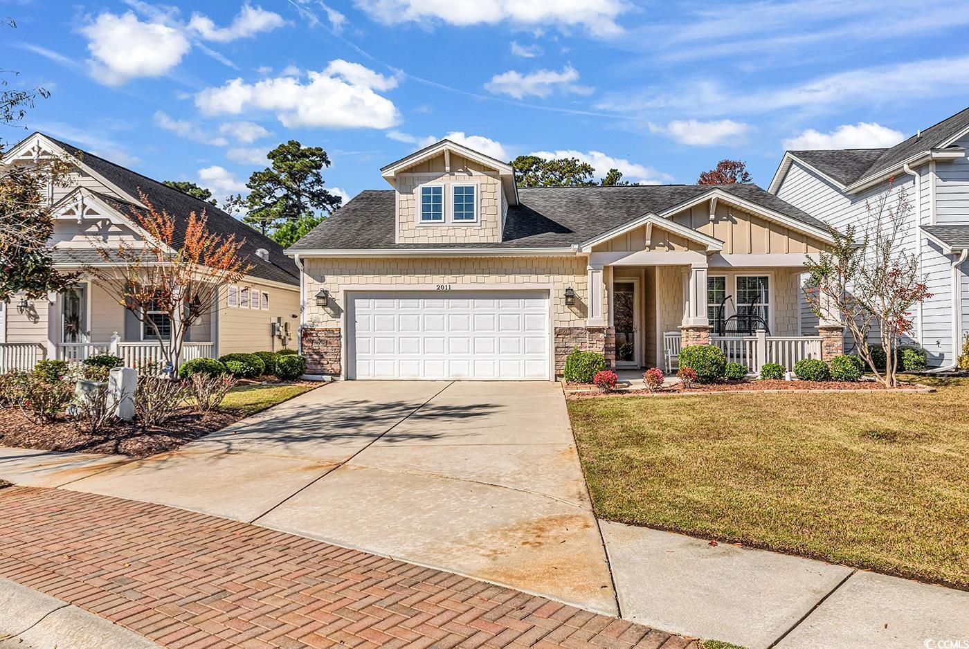 Craftsman inspired home with covered porch, roof with shingles, a front lawn, driveway, and stone siding