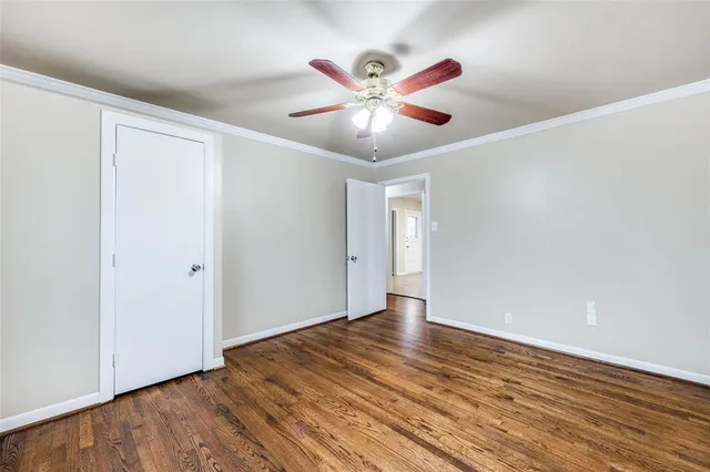 a view of an empty room with wooden floor and a ceiling fan