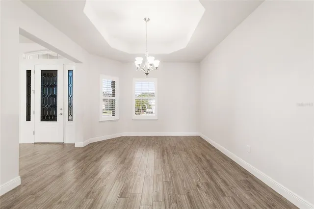 an empty room with wooden floor chandelier and windows