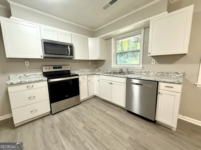 a kitchen with stainless steel appliances granite countertop white cabinets a sink a stove a microwave and wooden floors