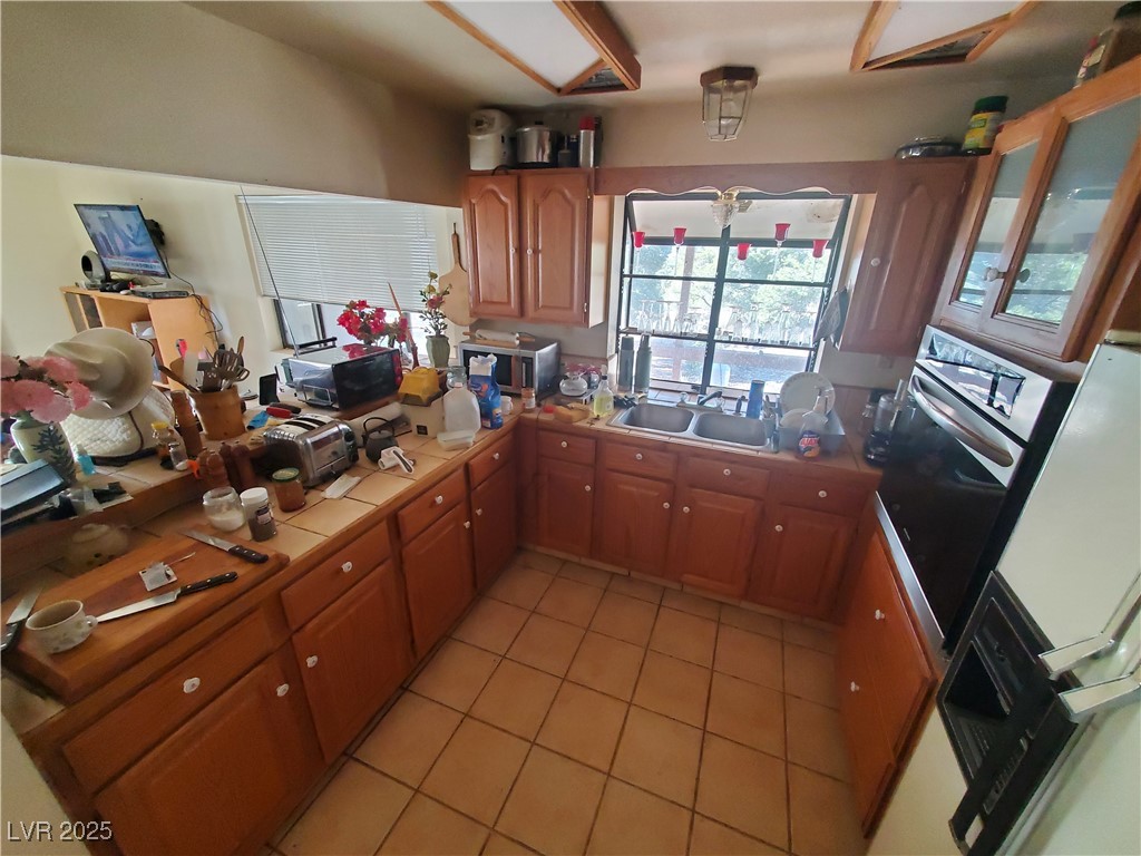1281 Meadow Lane Pioche, NV 89043 - Photo 11 of 34 Kitchen featuring light tile patterned flooring, a sink, tile counters, stainless steel microwave, and brown cabinets