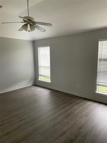 an empty room with wooden floor fan and windows