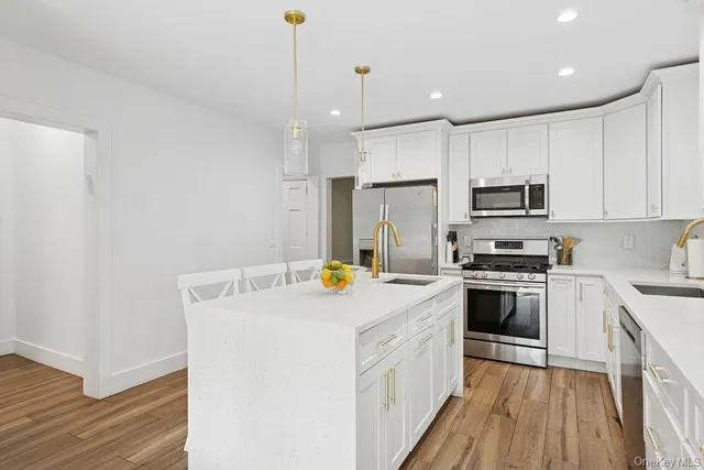 a kitchen with a stove a sink a refrigerator and white cabinets with wooden floor