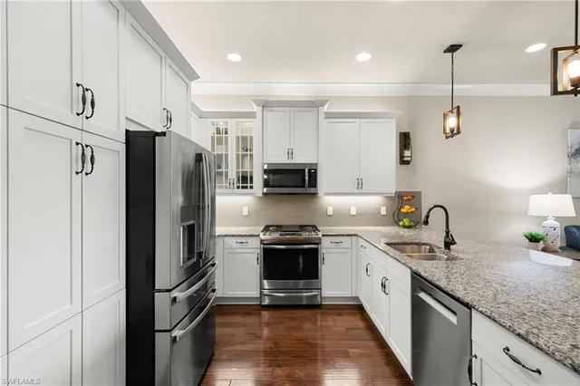 a kitchen with stainless steel appliances granite countertop a refrigerator a sink dishwasher a stove and white countertops with wooden floor