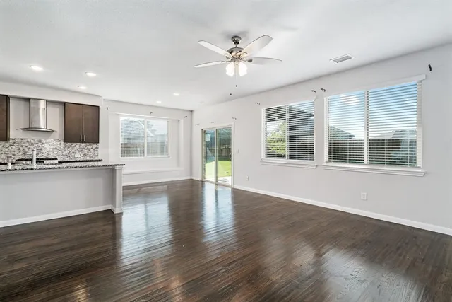 a view of an empty room with wooden floor and a kitchen