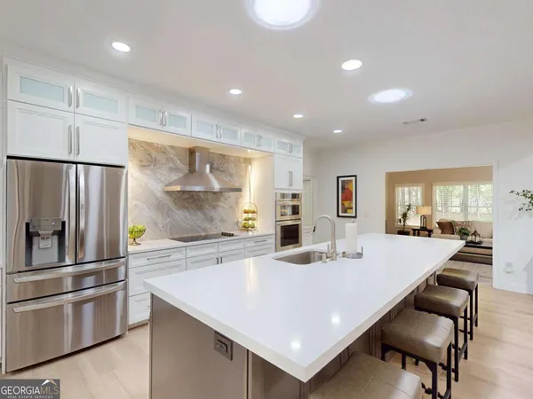 a large kitchen with kitchen island a stove a sink a refrigerator and white cabinets with wooden floor