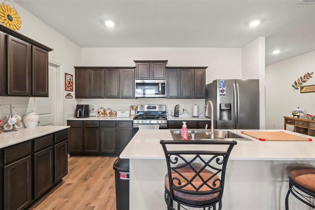 742 Buttercup Drive Pilot Point, TX 76258 - Photo 7 of 20 Kitchen featuring a breakfast bar area, appliances with stainless steel finishes, dark brown cabinetry, light wood-type flooring, and a kitchen island with sink