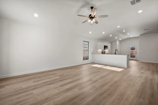 a view of a livingroom with a ceiling fan wooden floor and kitchen