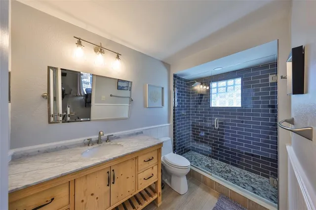 a bathroom with a granite countertop sink a toilet a mirror and shower