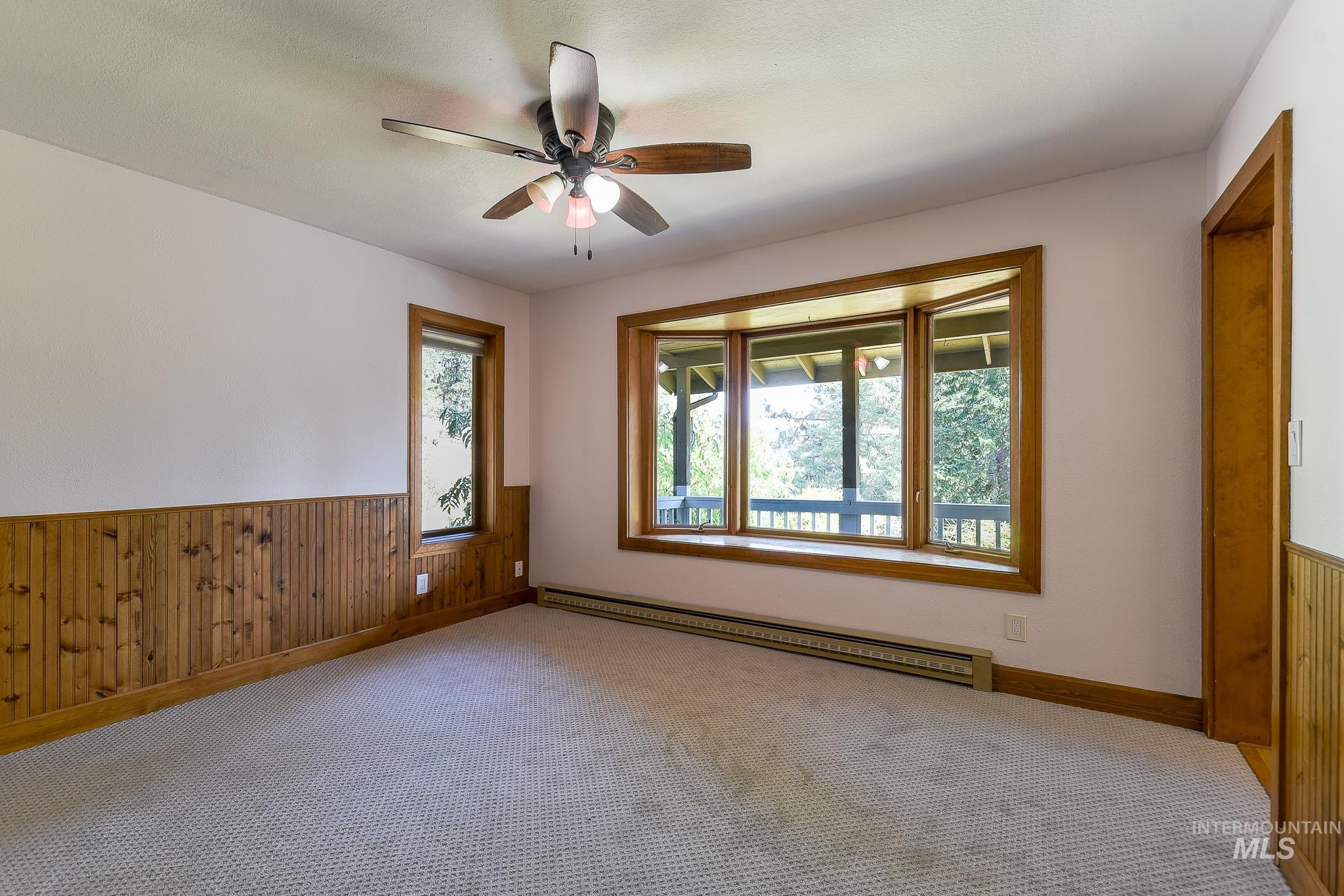 1045 Joyce Road Moscow, ID 83843 - Photo 15 of 50 Bay window with wood trim, wood paneling, ceiling fan with light fixture, and wall-to-wall carpeting