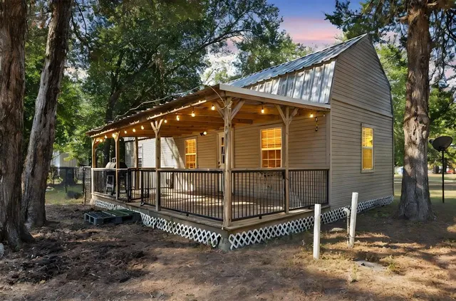 a view of a wooden house with a small yard and large trees
