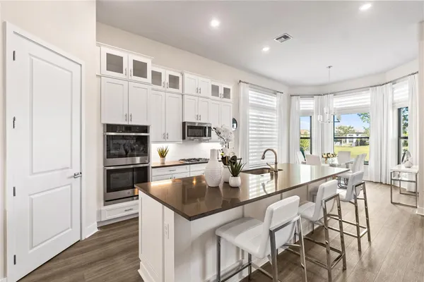 a kitchen with stainless steel appliances granite countertop a stove a sink a refrigerator white cabinets and wooden floor